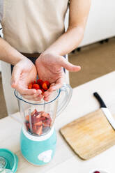Mann gibt frische gehackte Erdbeeren in den Mixer - GIOF11751