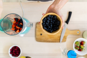 Man holding bowl of fresh blueberries in kitchen - GIOF11756