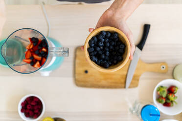 Mann hält Schüssel mit frischen Blaubeeren in der Küche - GIOF11756