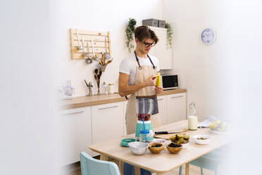 Junger Mann steht in der Küche und schält eine Banane für einen Smoothie - GIOF11759