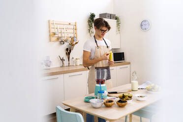 Young man standing in kitchen peeling banana for smoothie - GIOF11759