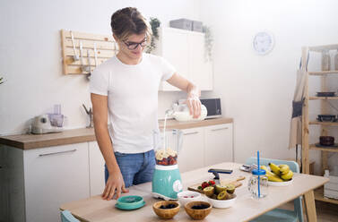Junger Mann gießt Milch in den Mixer, während er in der Küche einen Smoothie zubereitet - GIOF11771