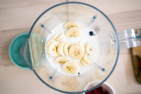 Frische Bananen und Milch im Mixer auf dem Tisch - GIOF11773