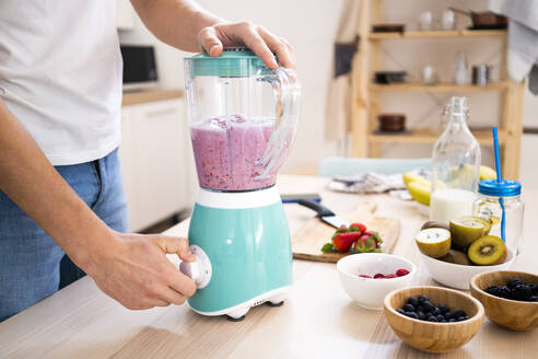 Man blending smoothie in blender on table in kitchen at home - GIOF11775