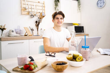 Young man with laptop sitting at table in kitchen - GIOF11787