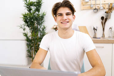 Smiling young man sitting in kitchen at home - GIOF11788