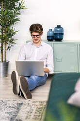 Junger Mann, der einen Laptop benutzt, während er zu Hause im Wohnzimmer sitzt - GIOF11812