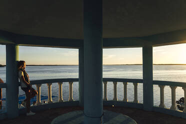 Weibliche Touristin lehnt an einer architektonischen Säule und betrachtet die Aussicht bei Sonnenuntergang - JMPF00884