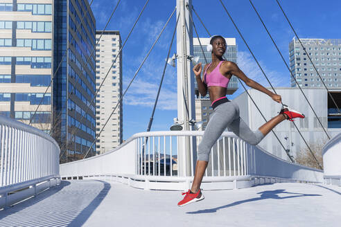 Fit woman jumping on bridge while listening music through headphones during sunny day - RFTF00005