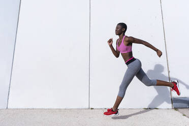 Smiling female athlete running against white wall - RFTF00015