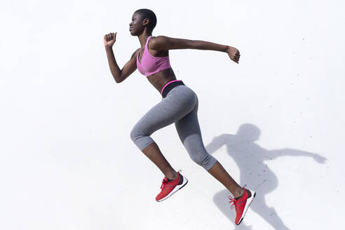 Female runner jumping while practicing against white wall - RFTF00018
