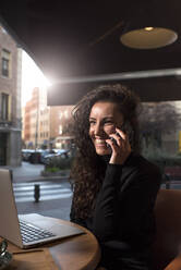 Fröhliche Frau, die in einem Café mit ihrem Handy telefoniert - DAMF00743