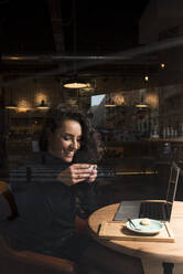 Smiling businesswoman drinking coffee sitting at cafe - DAMF00745