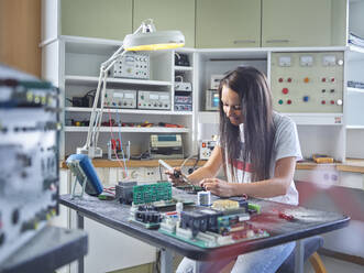 Smiling female electrician using soldering iron on circuit at electrical workshop - CVF01674