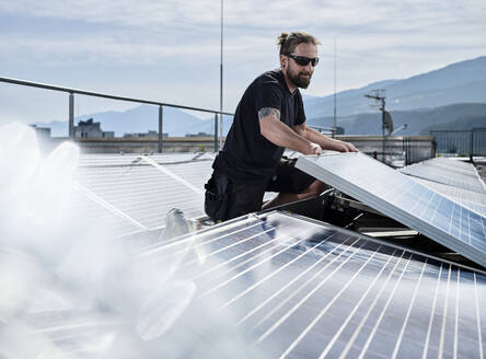 Männlicher Elektriker bei der Installation von Sonnenkollektoren auf der Terrasse eines Gebäudes an einem sonnigen Tag - CVF01675