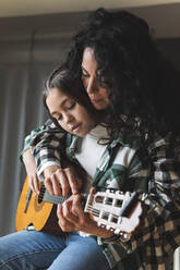 Mother teaching little daughter how to play acoustic guitar - JAQF00382