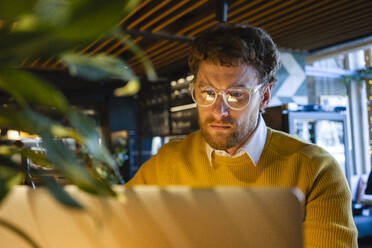 Männlicher Besitzer mit Brille arbeitet in einem Café am Laptop - VPIF03654