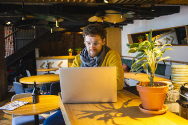 Gut aussehender Geschäftsmann, der einen Laptop benutzt, während er in einem Café sitzt - VPIF03657