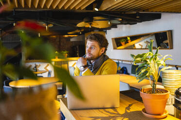 Nachdenklicher männlicher Besitzer mit Laptop, der wegschaut, während er im Cafe sitzt - VPIF03658