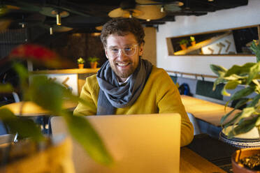 Glücklicher männlicher Besitzer mit Laptop im Cafe sitzend - VPIF03660