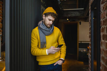 Businessman with hand in pocket using smart phone while leaning on railing in cafe - VPIF03664