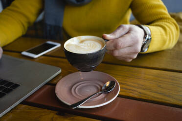 Mann hält Kaffeetasse am Laptop in einem Cafe - VPIF03673