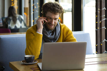 Gut aussehender Geschäftsmann, der in einem Café mit seinem Laptop telefoniert - VPIF03676