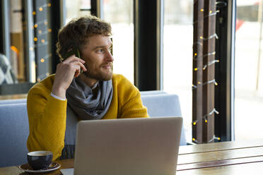 Contemplating businessman talking on smart phone while sitting with laptop at cafe - VPIF03677