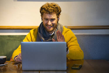 Smiling businessman gesturing during video call on laptop at cafe - VPIF03684