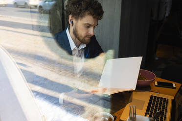 Male entrepreneur reading strategy during video call on laptop while sitting at cafe - VPIF03699