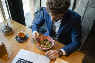 Geschäftsmann isst Salat, während er mit seinem Laptop in einem Café sitzt - VPIF03702