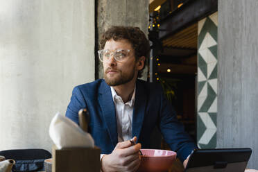 Nachdenklicher Geschäftsmann mit Brille, der wegschaut, während er in einem Café isst - VPIF03706