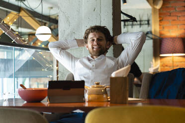 Relaxed businessman with hands behind head sitting at cafe - VPIF03711