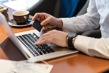 Man holding credit card for online payment through laptop at cafe - VPIF03714