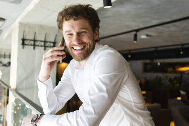 Cheerful businessman talking on mobile phone while leaning on railing at cafe - VPIF03719