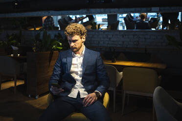 Männlicher Besitzer im Anzug, der ein Smartphone benutzt, während er in einem Cafe sitzt - VPIF03720