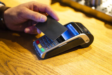 Man paying with credit card through reader machine at cafe - VPIF03724