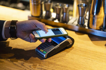Mann beim kontaktlosen Bezahlen mit seinem Smartphone über ein Kreditkartenlesegerät in einem Café - VPIF03725
