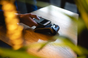 Man doing online payment through smart phone over credit card reader at cafe - VPIF03726