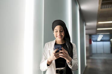 Junge Frau mit Kopftuch benutzt ein Smartphone in einem Einkaufszentrum - JCCMF01438
