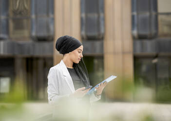 Young businesswoman wearing headscarf planning strategy while standing outdoors - JCCMF01447