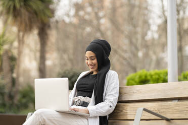 Beautiful Arab businesswoman working on laptop while sitting outdoors - JCCMF01459