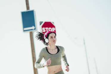 Woman with headphones looking away while running against sign board - JCMF01916
