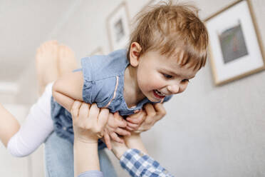 Verspielte Mutter, die ihre fröhliche Tochter hochhebt, während sie ihre Freizeit zu Hause verbringt - OGF00945