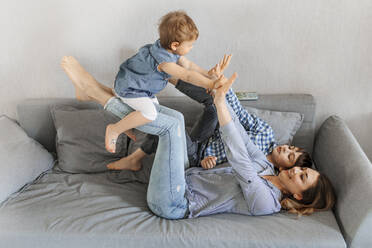 Mother lifting daughter by son on sofa at home - OGF00946