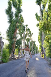 Greece, Dodecanese, Kolymbia, Adult woman hopping merrily along eucalyptus avenue in summer - ECPF01057