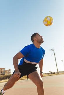 Mann köpft Ball beim Fußballspielen an einem sonnigen Tag - MIMFF00608