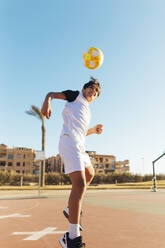 Boy heading soccer ball on sports court against sky - MIMFF00610