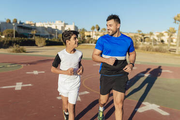 Lächelnder Vater sieht seinen Sohn beim Laufen auf dem Sportplatz an - MIMFF00613