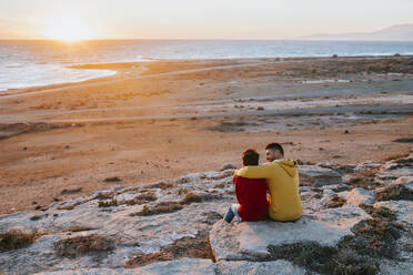 Vater und Sohn sitzen auf einem Felsen am Strand - MIMFF00625